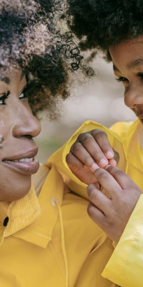 A parent and child in rain gear smiling at one another
